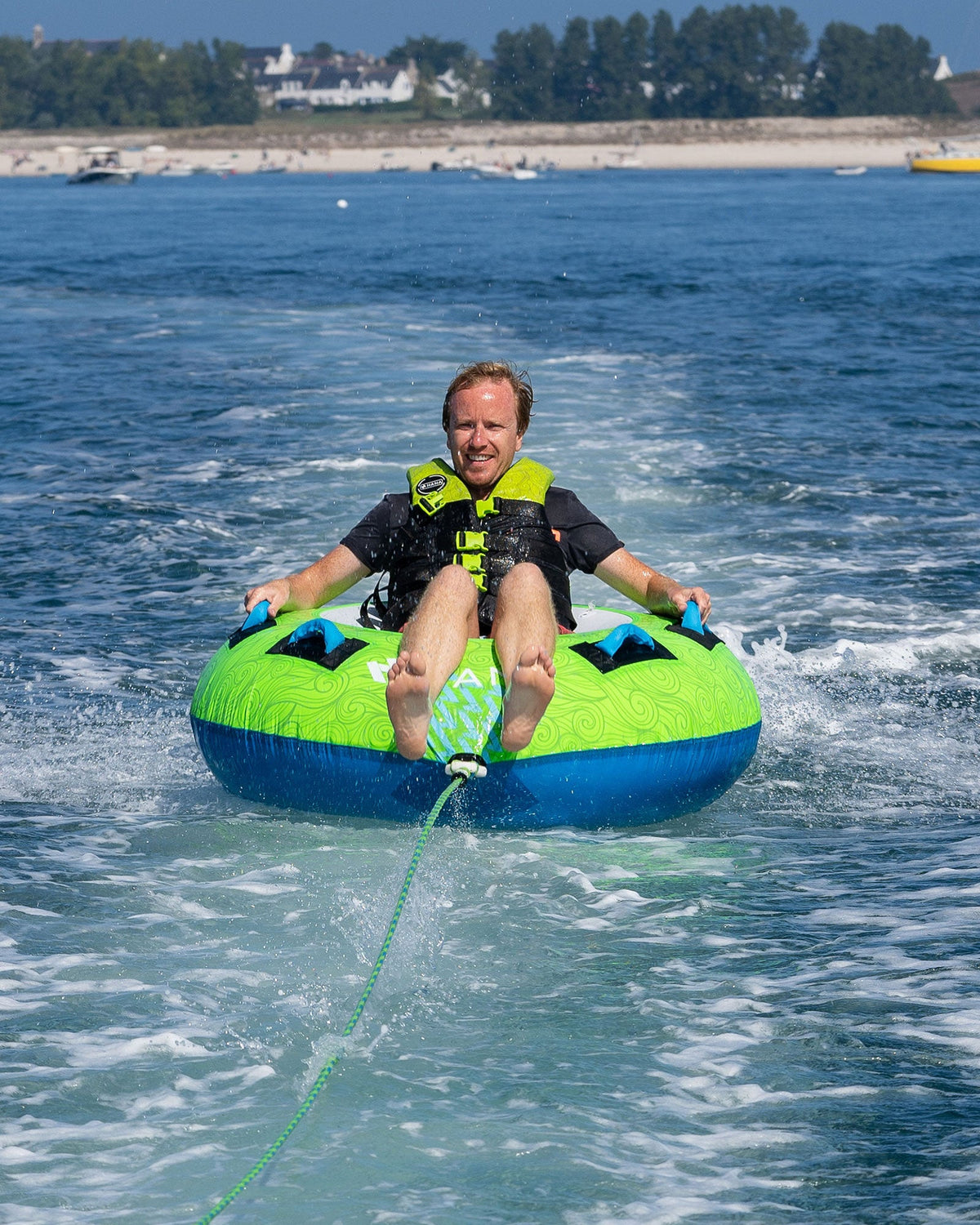 Man riding a green and blue HANA towable tube behind a boat