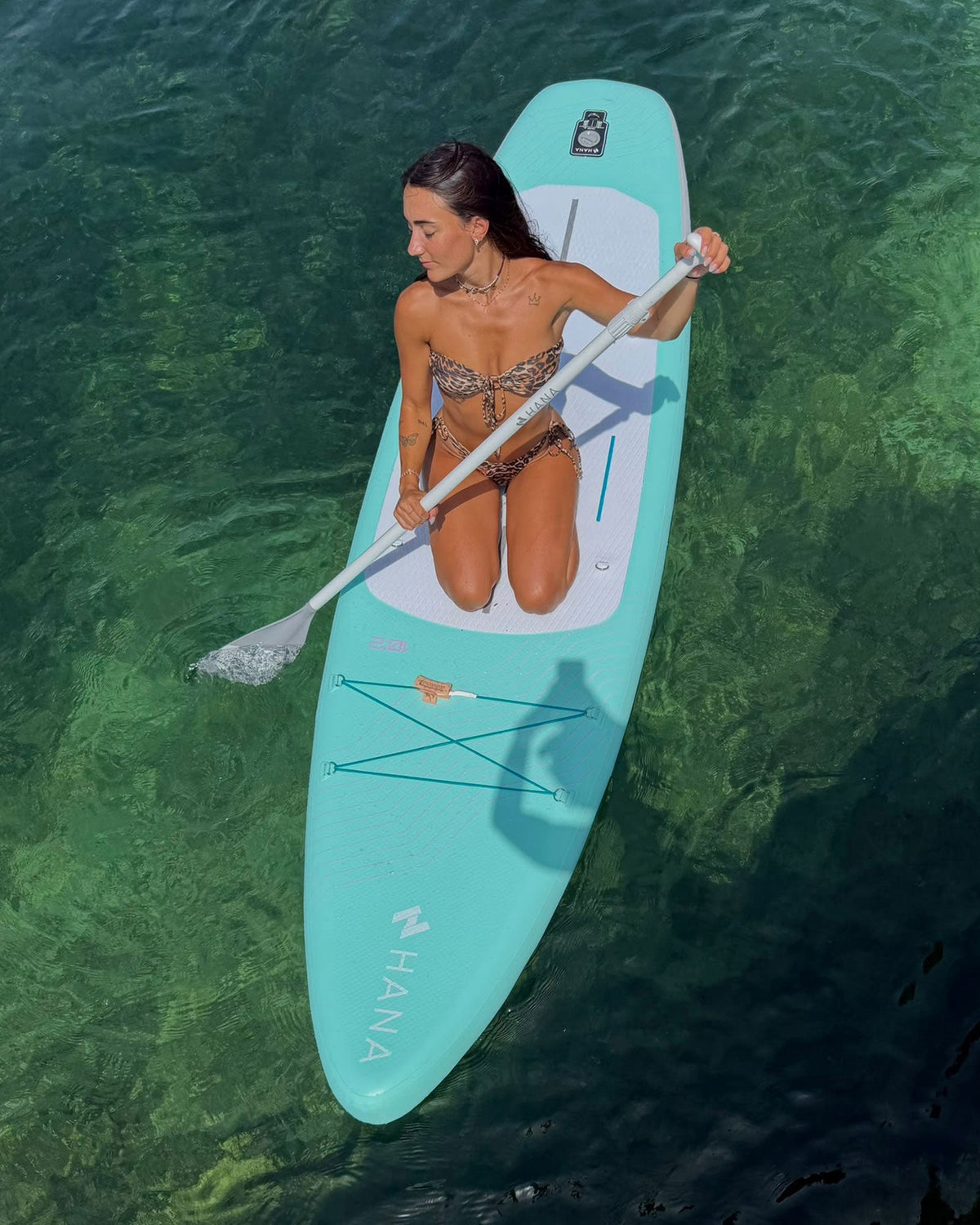 Femme à genoux sur un paddle gonflable HANA mint, vue du dessus sur une eau turquoise
