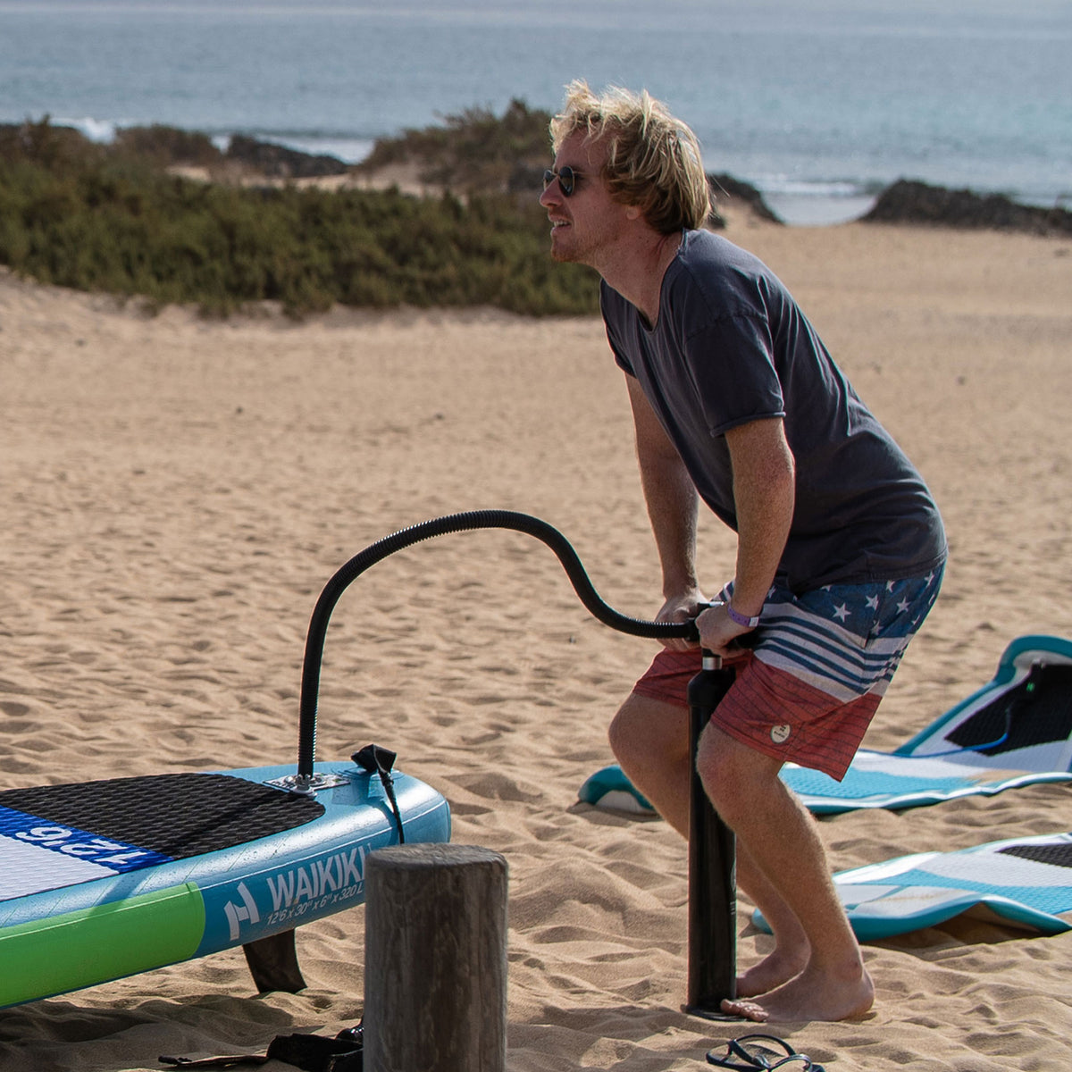 Homme gonflant un paddle avec la pompe double action HANA Premium sur la plage