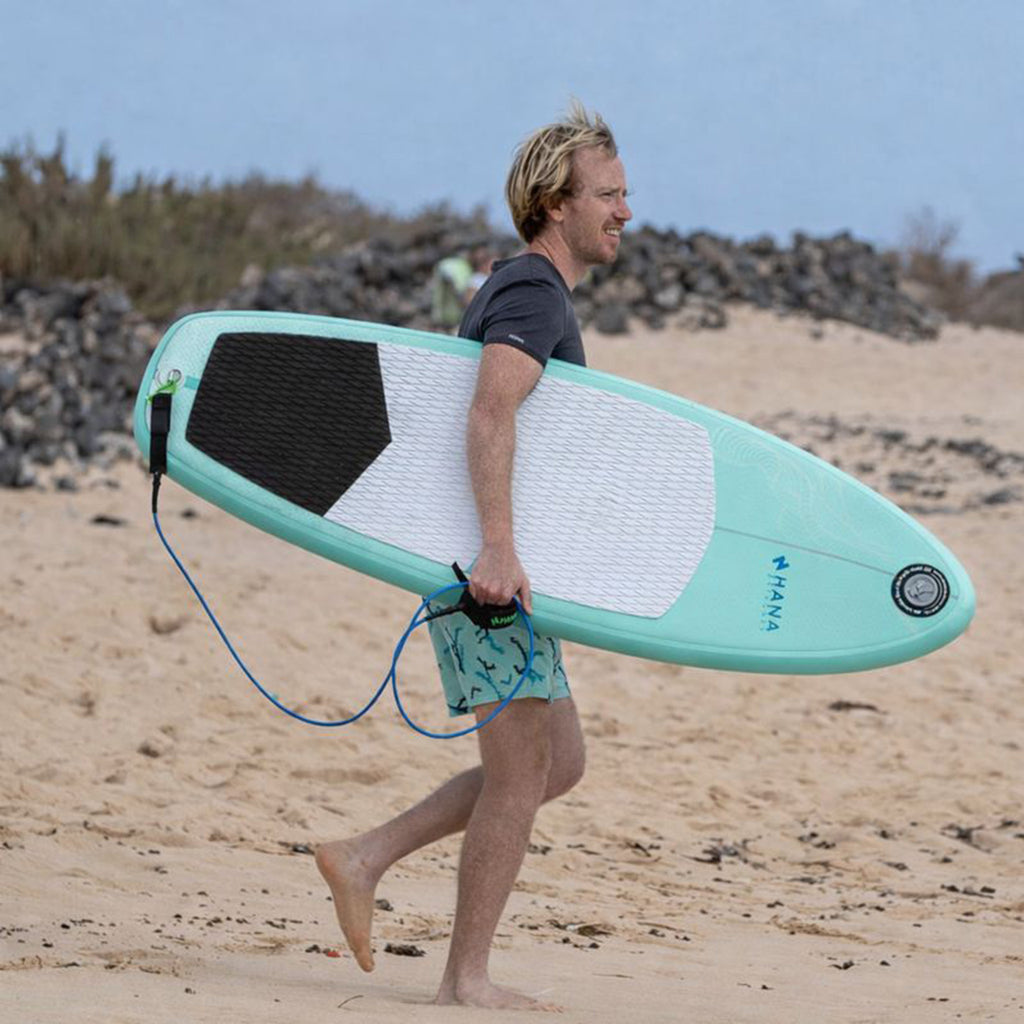 Surfeur sur la plage avec la planche de surf gonflable HANA Premium 5'4 sous le bras