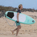 Surfeur sur la plage avec la planche de surf gonflable HANA Premium 5'4 sous le bras