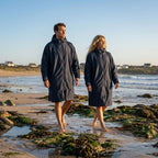 Couple walking on the beach at sunset, wearing the HANA navy blue waterproof poncho